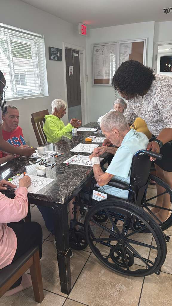 A caregiver assisting residents during a group coloring activity at the dining table at Atlantis Senior Care Residence