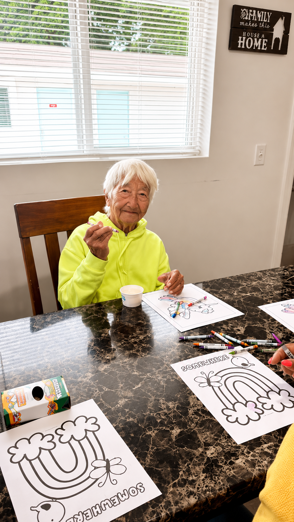 A smiling resident holding a crayon during a rainbow-themed coloring activity at Atlantis Senior Care Residence